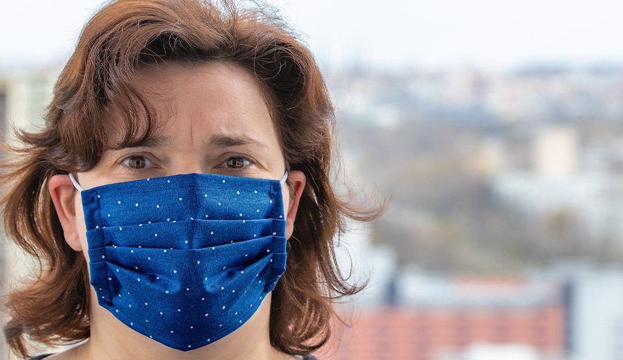 Woman wearing a blue fabric face mask, with a cityscape blurred in the background and a child nearby offering assistance.