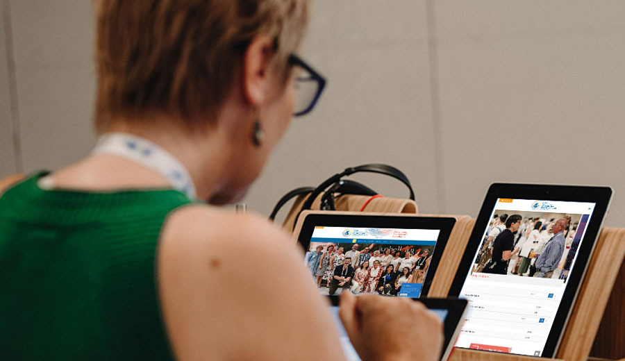 A woman at a conference edits photos on a tablet, displaying one with her family on the screen.