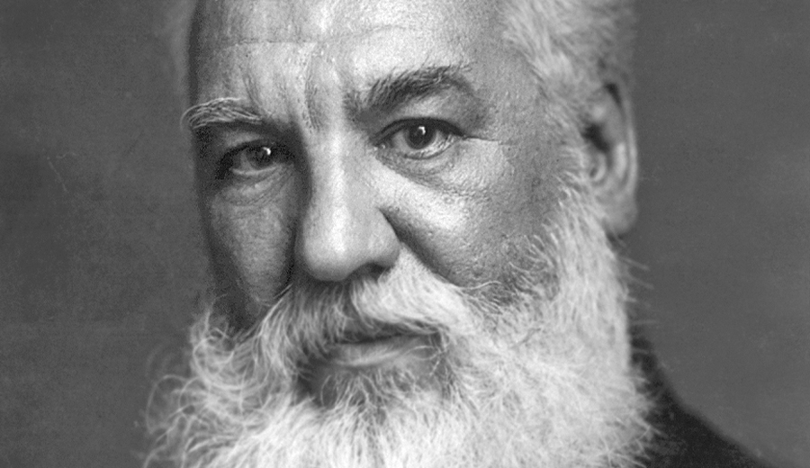 Black and white portrait of an elderly man with a full white beard and hearing assistance device, looking directly at the camera.