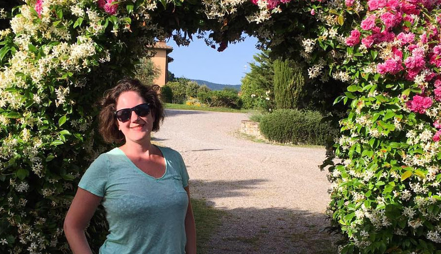 woman in t-shirt standing under arch of pink flowers
