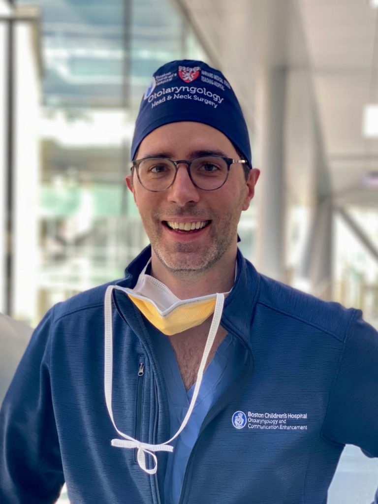 A smiling male doctor wearing scrubs, a surgical cap labeled “otolaryngology,” and a badge from Boston Children's Hospital.