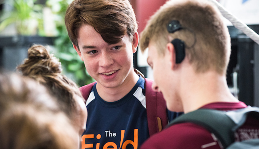 A teenage boy smiling at peers during a conversation in a school setting.