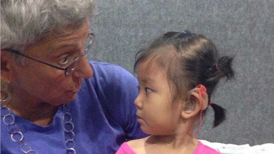 Elderly woman in a blue blouse and young child in a pink shirt engaging in a close conversation, eye-to-eye.