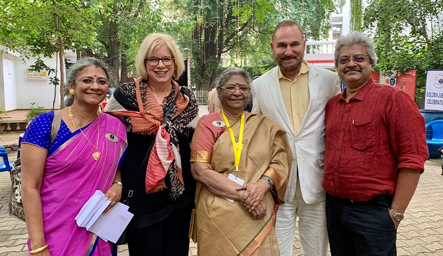 Five family members smiling for a group photo, three women and two men, with trees and a building in the background.