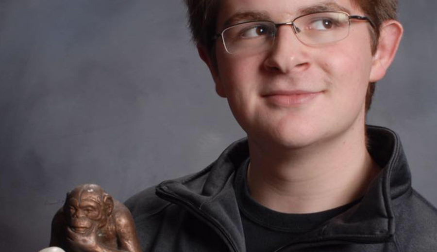 Young man with glasses holding a small statue of a monkey, smiling gently at the camera with his family around him.
