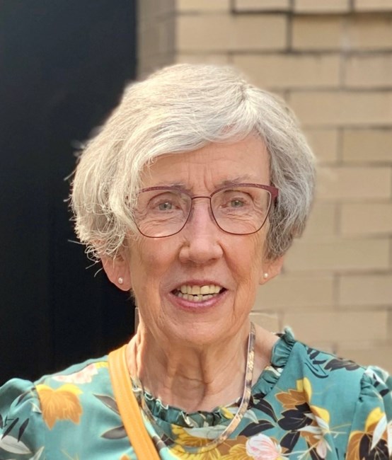 An elderly woman with short gray hair and glasses, smiling in a floral top, standing outdoors with a child.