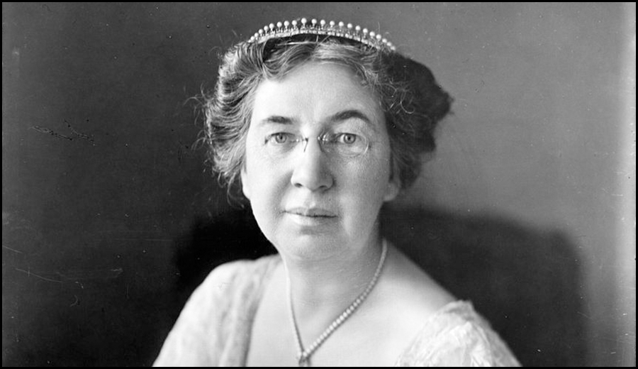 Black and white portrait of an elderly woman with glasses, wearing a tiara and a light-colored dress, looking directly at the camera, radiating the warmth of family.