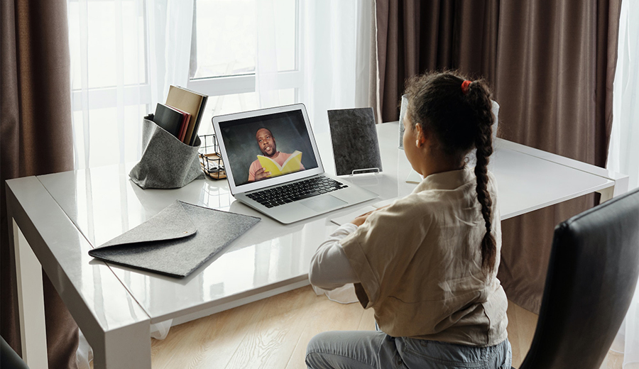 Young girl sitting at a desk, using a laptop for a video call with her family member, a smiling grownup man displayed on the screen.