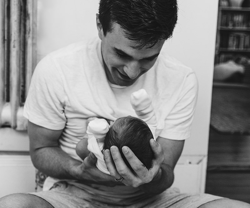 Black and white photo of a smiling man holding a newborn child in his hands.