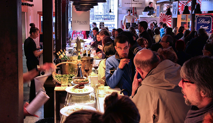 Crowded family street food market with people eating and vendors serving food at night.